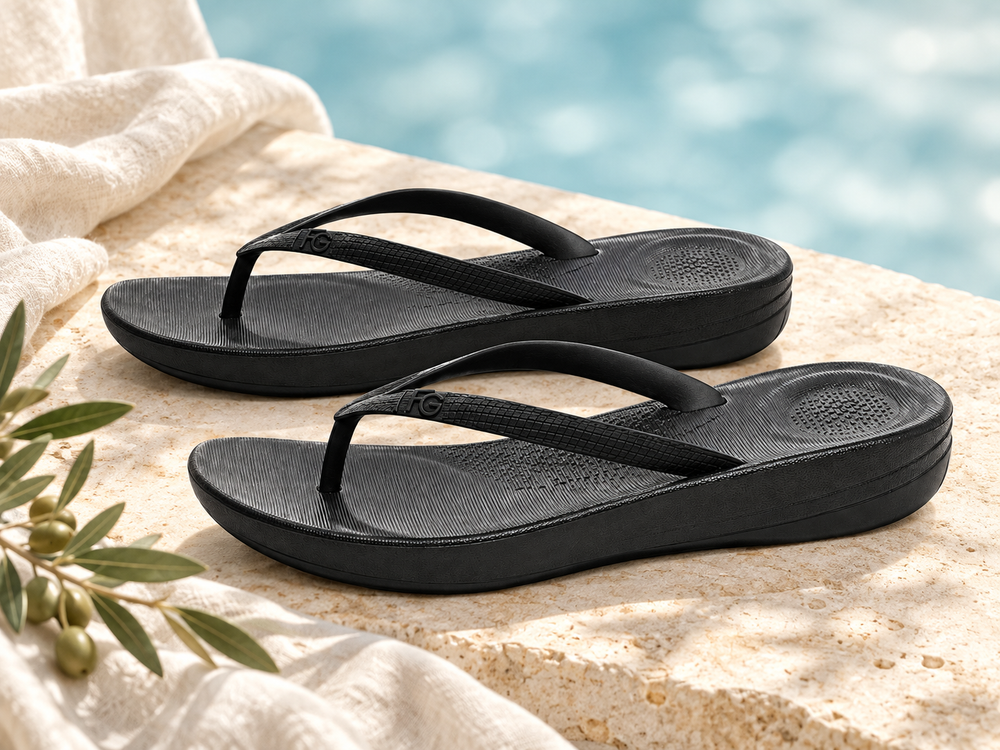 Black flip-flops on warm stone beside ivory linen