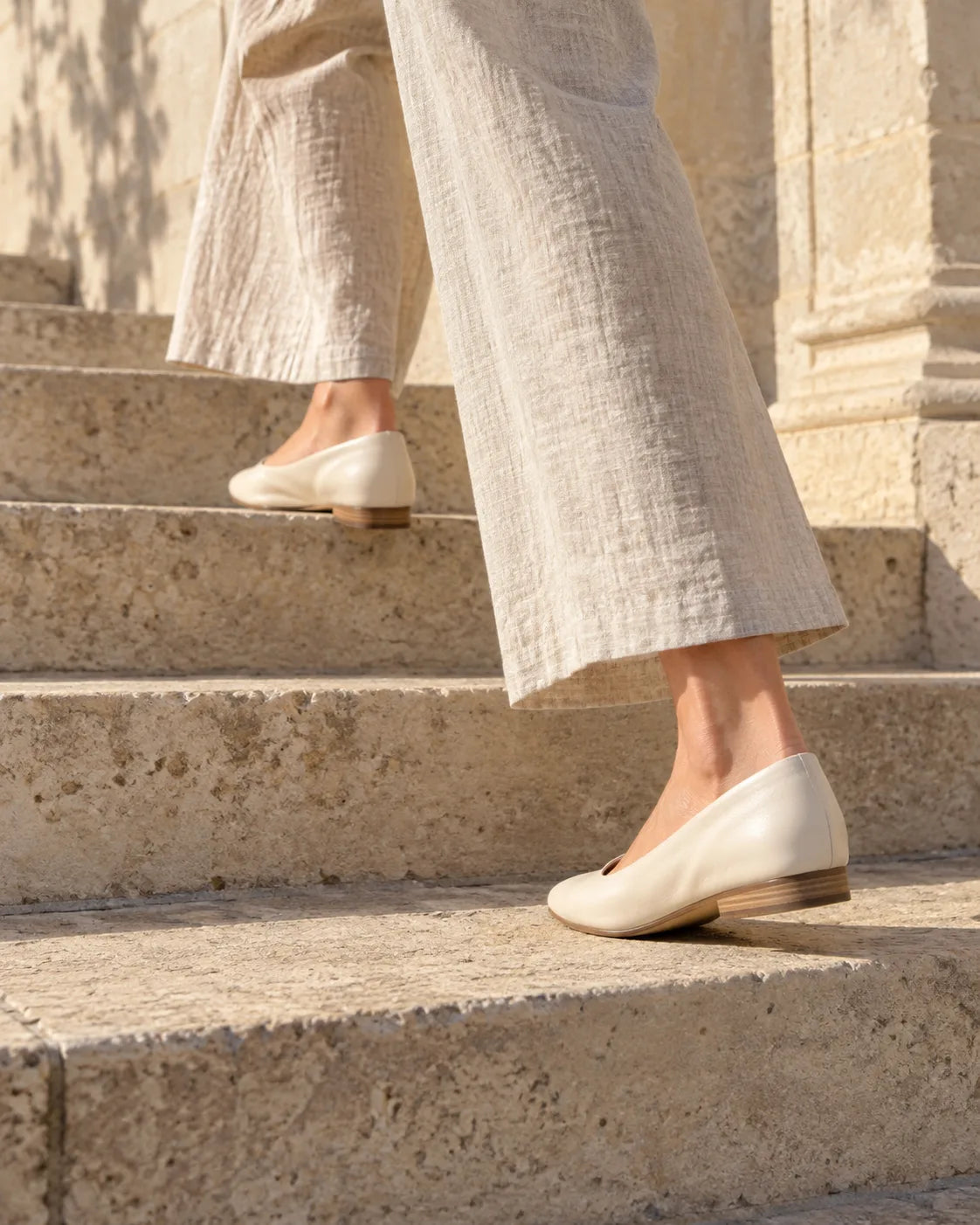 Neutral footwear and linen trousers in a sunlit architectural setting